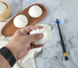 Macro view of squeezing a realistic white steamed bun squishy toy on a bamboo steamer