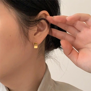 Close-up of minimalist gold rectangular stud earrings with UA engraving on a female model