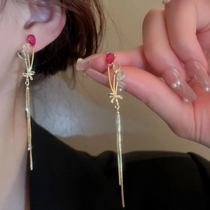 Detail of long gold tassel earring with red waterdrop zircon and bowknot on a model