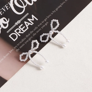 Detail view of handmade bow-shaped imitation pearl earrings on a stylish magazine backdrop