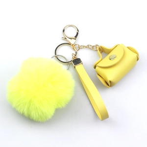 Detail of yellow plush pom-pom and mini leather handbag keychain with gold metal buckle