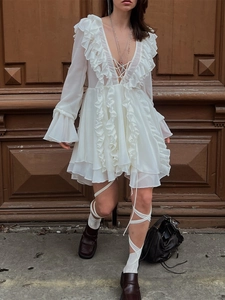 White V-neck chiffon dress with long sleeves and ruffled hem on dark wooden background