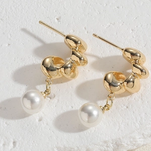 Close-up of golden irregular metal earrings with white pearls on a stone texture