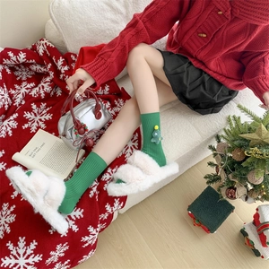Detail of green knit Christmas socks with tree decor and white plush slippers