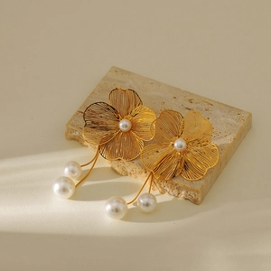 Detail of gold floral tassel earrings with pearls resting on a textured stone base
