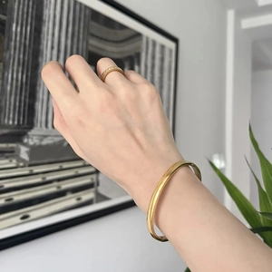Bracciale rigido dorato lucido e anello con strass indossati da una modella in un set elegante