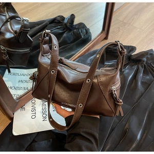 Detail of dark brown leather tote featuring wide straps with metal eyelets and knotted zippers
