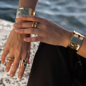 Golden chunky cuff bracelet and statement rings on hand with water background