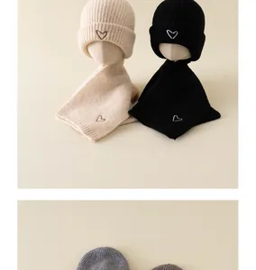 Detail of knitted baby hat and scarf set featuring delicate heart embroidery in beige and black