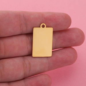 Polished gold rectangular stainless steel pendant held by hand on pink background