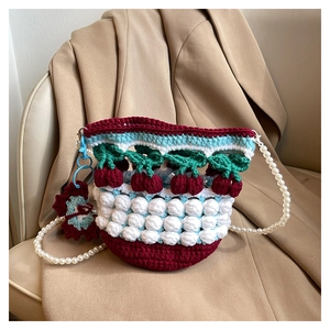 Detail of crochet bucket bag with red cherry accents and elegant pearl shoulder strap