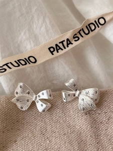 Close-up of silver bow earrings with sparkling cubic zirconia on soft beige fabric