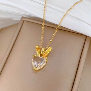 Detail of a gold titanium necklace with a heart-shaped crystal pendant on a soft background
