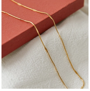 Macro shot of gold stainless steel wave chain necklace with detailed texture on red fabric