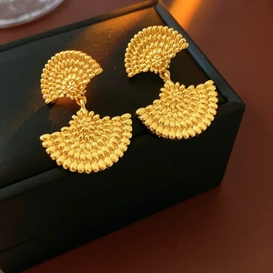 Détail de boucles d'oreilles vintage dorées en forme d'éventail avec texture sur boîte noire