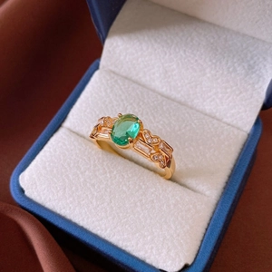 Close-up of gold ring with oval green gemstone and heart-shaped side accents in velvet box