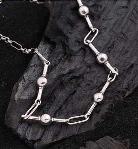 Detailed view of a silver bead chain bracelet on a black textured background