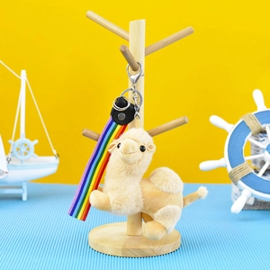 Detailed view of a plush camel keychain pendant featuring a rainbow ribbon on a wooden stand