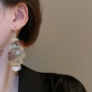 Close-up of layered silver petal tassel earrings worn by a model in black clothing