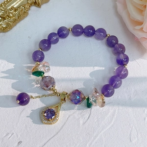 Detail of natural amethyst bracelet with crystal flower charms on textured white surface