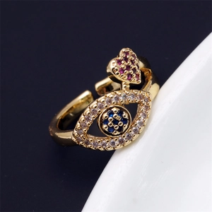 Détail macro d'une bague œil dorée avec zircon bleu et breloque cœur rose