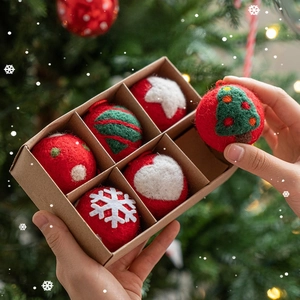 Hand holding a gift box with 6 red wool felt Christmas tree ornaments in festive setting