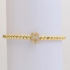 Close-up of golden beaded stretch bracelet with a micro-pave cubic zirconia letter H charm