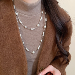 Close-up of long layered pearl necklace on brown wool coat and camel turtleneck