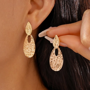 Close-up of golden geometric water drop earrings with irregular textured hammer finish