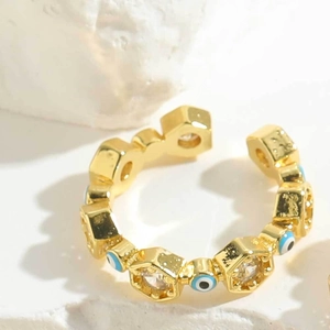 Detailed view of gold evil eye ring with blue zircons on white textured stone