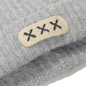 Dettaglio macro della trama in maglia grigia del cappello con toppa ricamata tripla X