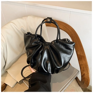 Detailed shot of black pleated cloud bag with soft faux leather texture on wooden seat