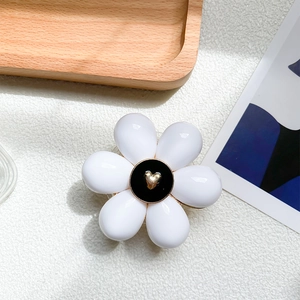 Detail shot of white resin flower phone grip with black center and golden heart on a tray