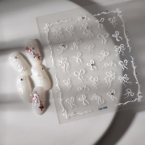 3D white bow nail stickers with embossed ribbon patterns and miniature rhinestones