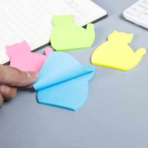 Detail of colorful cat-shaped sticky notes on a desk with a finger peeling a blue sheet