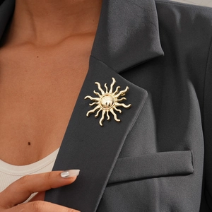 Detail of a gold sun-shaped brooch pinned on a dark grey suit lapel for a formal look