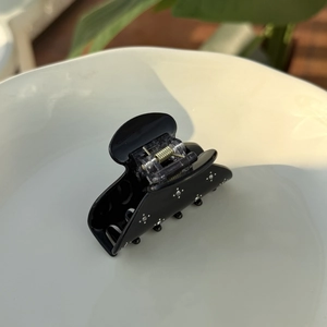 Detail of glossy black acetate hair claw clip with rhinestones on a white ceramic plate