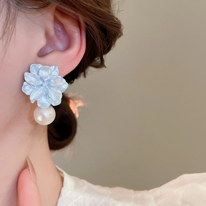 Close-up of light blue flower earrings with white pearl pendants worn by a model