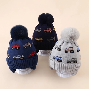 Close-up of children's tractor pattern knit earflap hats with plush faux fur pom-poms
