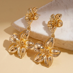 Close-up of golden metallic floral drop earrings on white stone with high-end texture