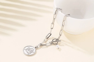 Silver paperclip necklace with angel coin pendant and pearl detail in soft lighting