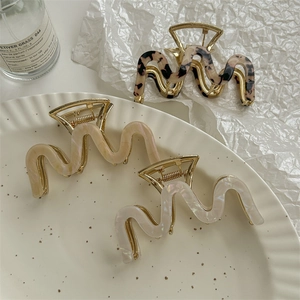 Three wave-shaped hair claws in tortoiseshell, cream, and pearl white colors