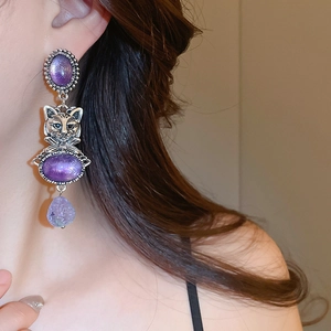 Macro view of vintage silver cat earrings featuring purple gemstones and drop pendants