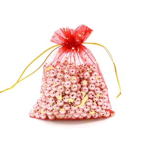 Detail of red organza gift bag with gold star moon pattern filled with pink faux pearls