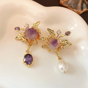 Asymmetric butterfly earrings with purple gems and white pearls on ceramic tray