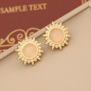 Macro shot of sunburst gold earrings with translucent pink stone on a beige leather tray