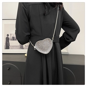 Close-up of heart-shaped silver rhinestone purse with thin chain on black dress