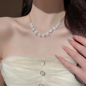 Detail of floral necklace featuring white daisy charms and sparkling crystals on model