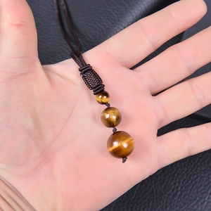 Tiger eye stone bead pendant necklace on brown braided cord shown in hand for scale