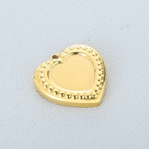 Macro view of a gold heart-shaped pendant with beaded edges on a textured grey background